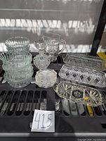Overview photo showing all glass items including stacked dessert bowls, perfume bottle, coasters, pitcher, and butter dishes