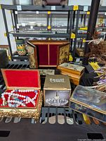 Photo of assorted jewelry boxes including brass floral box with red velvet interior, wooden boxes with floral and Hummel-style designs, boxed crystal ring holder, and decorative boxes.