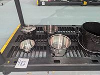 Various stainless steel camp cooking pots and bowls with foldable handles and a lid, displayed on a metal shelf.