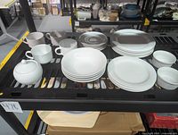 Photo showing the lot of Noritake Arctic White contemporary fine china on shelving, including mugs, saucers, sugar bowl, bowls, large and small plates, and ramekins arranged together.
