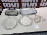 Overview photo of all glass bakeware and bowls showing two pie plates, two casserole dishes, and three apple-shaped glass bowls arranged on table.