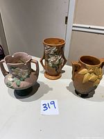 Three Roseville Pottery USA vases arranged on white surface showing different angles and overall condition.