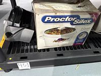 Proctor Silex slow cooker in original box next to Oster waffle maker with power cord coiled.