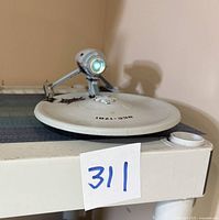 Overall side view of the USS Enterprise model showing front circular saucer section marked NCC-1701, mounted on a grey and black base surface.