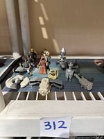 Overall view of 6 Star Wars figures and 7 accessory items laid out on a surface. Figures include stormtrooper-like and Jawa-like characters; accessories include ships and weapons. Items show wear.
