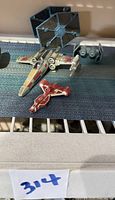 Three small Star Wars spacecraft including X-wing, red Republic fighter, and TIE Fighters on a surface showing size and condition