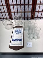 View of the entire lot including wall hanging, ice buckets, and glasses on a white table.