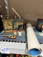 Front view of lot including carriage clock, card shuffler box, small wooden ukulele, Aunt Jemima bank, salt shaker and visible poster rolled on the side