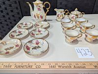 Full lot layout showing all pieces: footed coffee pot with lid, sugar bowl with lid, creamer, six cups, and six saucers decorated with pink roses, gold leaves, and iridescent finish
