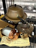 Photo showing full lot: Culinox copper fondue pot, small copper teapot, and vintage Mirro cookie press in original box, all with visible patina.