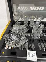 Photo showing various clear crystal items including vases, a decorative bowl, and butter dish on a black metal surface.