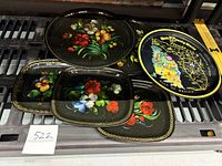 Six vintage hand painted metal trays displayed together, showing three circular floral trays, three rectangular floral trays, and the Walt Disney World tray.