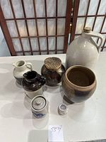 Full set of seven vintage stoneware pottery pieces, varying sizes, colors, some with cork lids, on white table