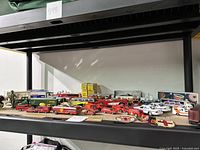 Wide angle photo of various vintage Matchbox cars and trucks organized on a shelf with some packaging boxes in the background