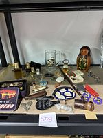 Wide image showing the full collection of vintage nicknacks on a table, including cologne bottles, Dale Earnhardt mug, Matryoshka doll, cutter, pipe, keychains and more.