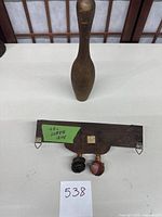 Front view of vintage wooden bowling pin and small wooden shelf bottom side with labels and hanging hooks