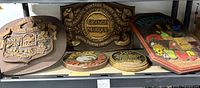 Photo showing five assorted vintage wooden signs placed on a shelf, including a shield-shaped Duff Gordon Sherries sign, a Grande Marque French wine sign, and colorful fish design plaque.