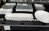 Full shelf view of all white Corelle tableware showing stacked rectangular plates, square plates, and four round white bowls placed in front.