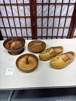 Photo showing the pair of wooden clogs and three different wooden bowls on a table in front of a folding screen.