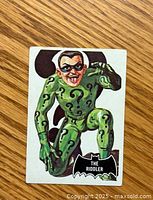 Front of 1966 Batman trading card showing The Riddler artwork in green costume with question marks.