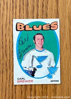 Front side of 1971-72 Carl Brewer hockey card showing portrait of player in Blues uniform and autograph present.