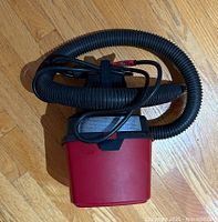 Side view of red and black shop vacuum with attached coiled flexible hose and power cord coiled on top of unit.