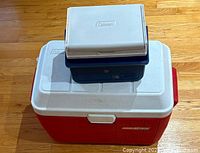 Photo of two Coleman coolers stacked, larger red and white cooler on bottom and smaller blue and white cooler on top.