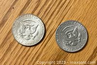 Two US half dollar coins, reverse side with presidential eagle seal visible, one in brighter silver tone, the other darker.