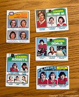 Front view of 5 hockey leader cards from 1976-77 O-Pee-Chee series, showing player images, teams, and statistical categories including goals, assists, and goals against average.