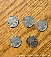 Five Buffalo Head Nickels laid out on a wood surface showing Native American profile side