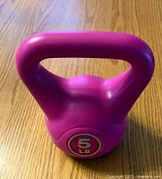 Photo of a purple 5 pound kettlebell with a wide handle and smooth surface, sitting on a wooden table.