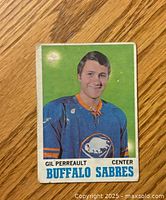 Front side of vintage OPC hockey card showing Gilbert Perreault in Buffalo Sabres jersey with some edge wear and crease.