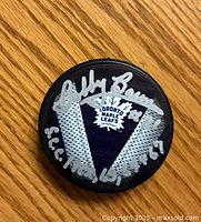 Top side of the hockey puck showing the Toronto Maple Leafs logo and Bobby Baun's silver autograph with inscription 'S.C.C. 1967'.