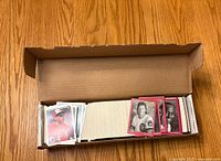 Open cardboard box filled with assorted baseball cards, visible front cards showing various players, some with red borders and Chicago Cubs logo.