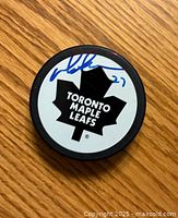 Toronto Maple Leafs hockey puck top side showing team logo and Darryl Sittler autograph in blue marker.
