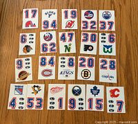 Top side of the 21 hockey emblem stickers spread out on a wooden surface showing all team logos and associated numbers.