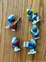 Top view of all five vintage Smurf figurines on wood surface, showing details and paint colors.