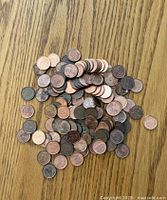 A pile of assorted pennies, showing a variety of wear and oxidation levels on a wood grain surface.