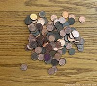A pile of mixed U.S. pennies in varying conditions spread on a wooden surface.