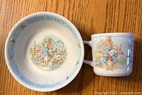 Front view of Peter Rabbit ceramic bowl and matching cup with colorful illustrations and text.