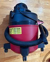 Front view of red and black Shop-Vac vacuum with hose wrapped around the base and caster wheels visible.