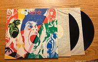 Photo showing the front of the UFO "Strangers In The Night" album cover with one vinyl record partially pulled out from its inner sleeve beside the cover on a wooden surface.