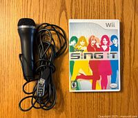 Wired USB microphone placed next to Disney Sing It Wii game case with cover art visible on wooden surface.