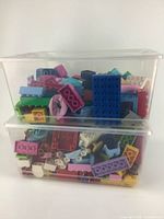 Photo of two stacked clear plastic bins containing assorted large size Lego style building blocks in various pastel and bright colors
