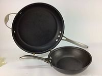 Two Calphalon frying pans, one larger and one smaller, showing black nonstick surfaces and aluminum handles with rivets.