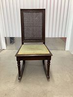 Full front view of the antique rocking chair showing cane back and seat, wooden frame and rockers.