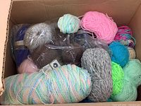 Box filled with assorted yarn balls and skeins in pastel and bright colors, some wrapped in plastic.