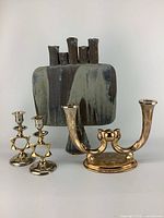 Front view of the three pieces: tall ceramic vase with a hand made look and two pairs of metal candle holders in brass and silver tones.