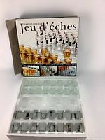 Front view of the Jeu d'éches box and open plastic chessboard insert with glass shot glasses inside.