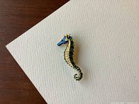 Top view of seahorse pin placed on a white textured surface showing detailed enamel colors and crystal accents.